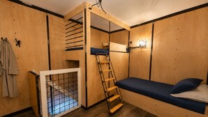 Een kleine kamer met een stapelbed, een trapje, een klein raam en een deur met een rasterpatroon.