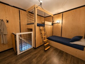 Une petite pièce comprenant un lit superposé, une échelle, une petite fenêtre et une porte à motifs géométriques.