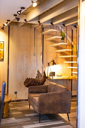 Un salon moderne avec un fauteuil suspendu, un canapé et un escalier agrémenté d’une plante.
