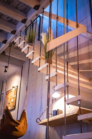 Un escalier en bois, avec un hamac et des plantes suspendues.