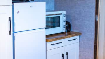 A compact kitchen with white cabinetry, a built-in microwave, and a coffee maker on the countertop.