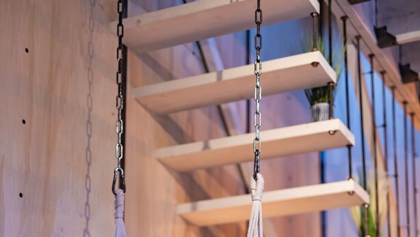 A hanging chair suspended from the ceiling, a wooden wall, and a sofa in a room. - Bay Terminus - The Hanging Lodge (Saint-Blimont)