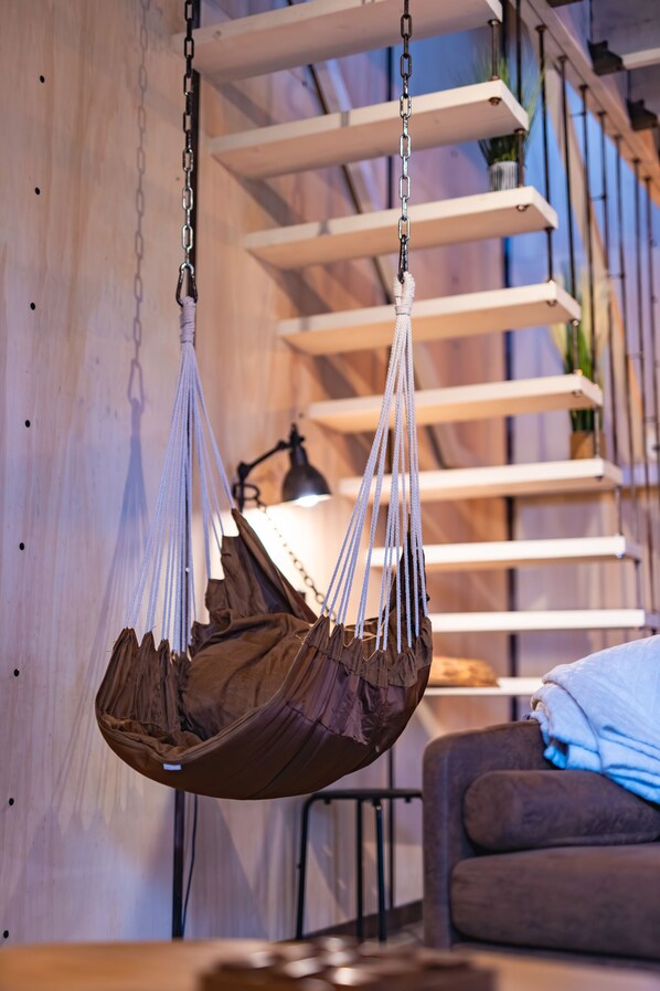A hanging chair suspended from the ceiling, a wooden wall, and a sofa in a room.