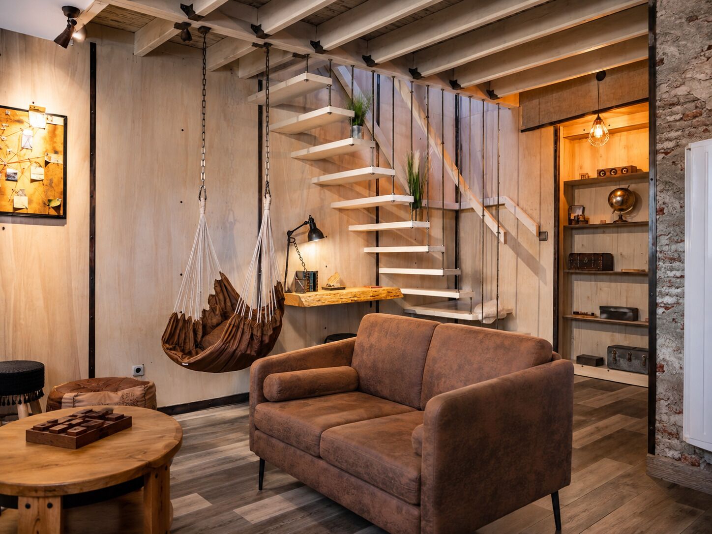 A modern interior with a hanging chair, a sofa, a round wooden table, and a spiral staircase.