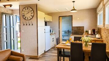 A modern kitchen with a dining area, featuring a clock, wooden flooring, and a sofa.