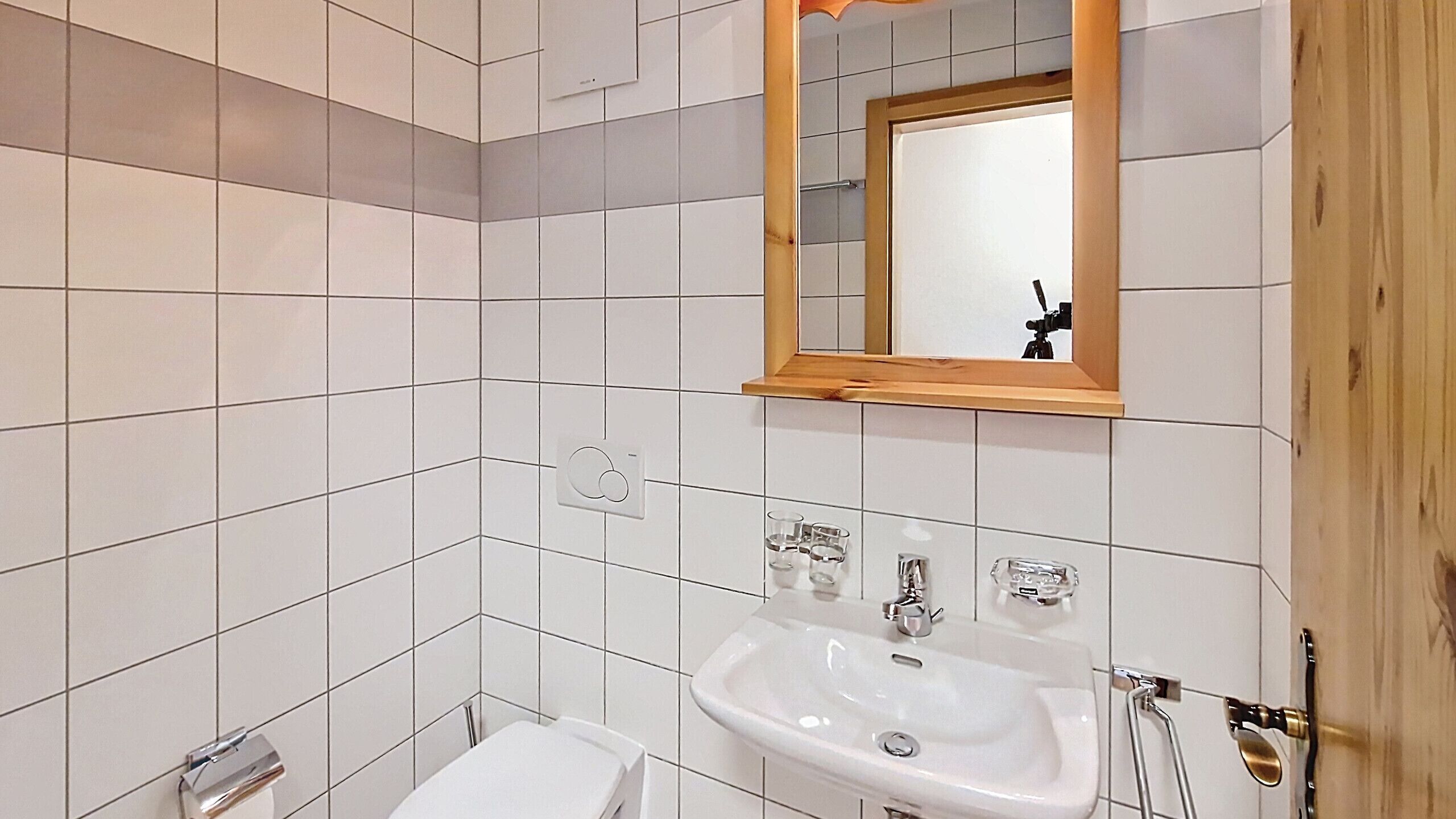 A bathroom with white tiles, a sink, a mirror, and a toilet.