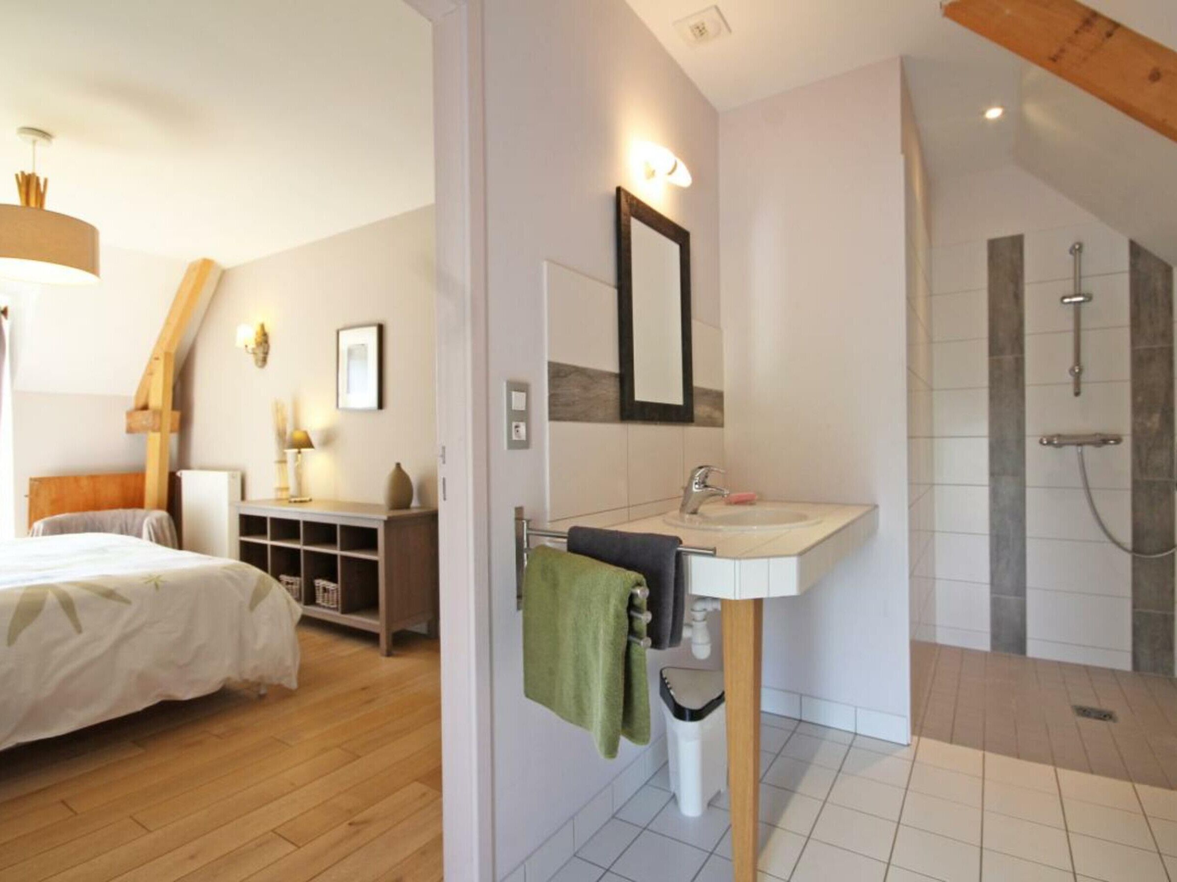 Un dormitorio con cama, mesita de noche y tocador. Cuenta con un baño que incluye lavabo, espejo y ducha.