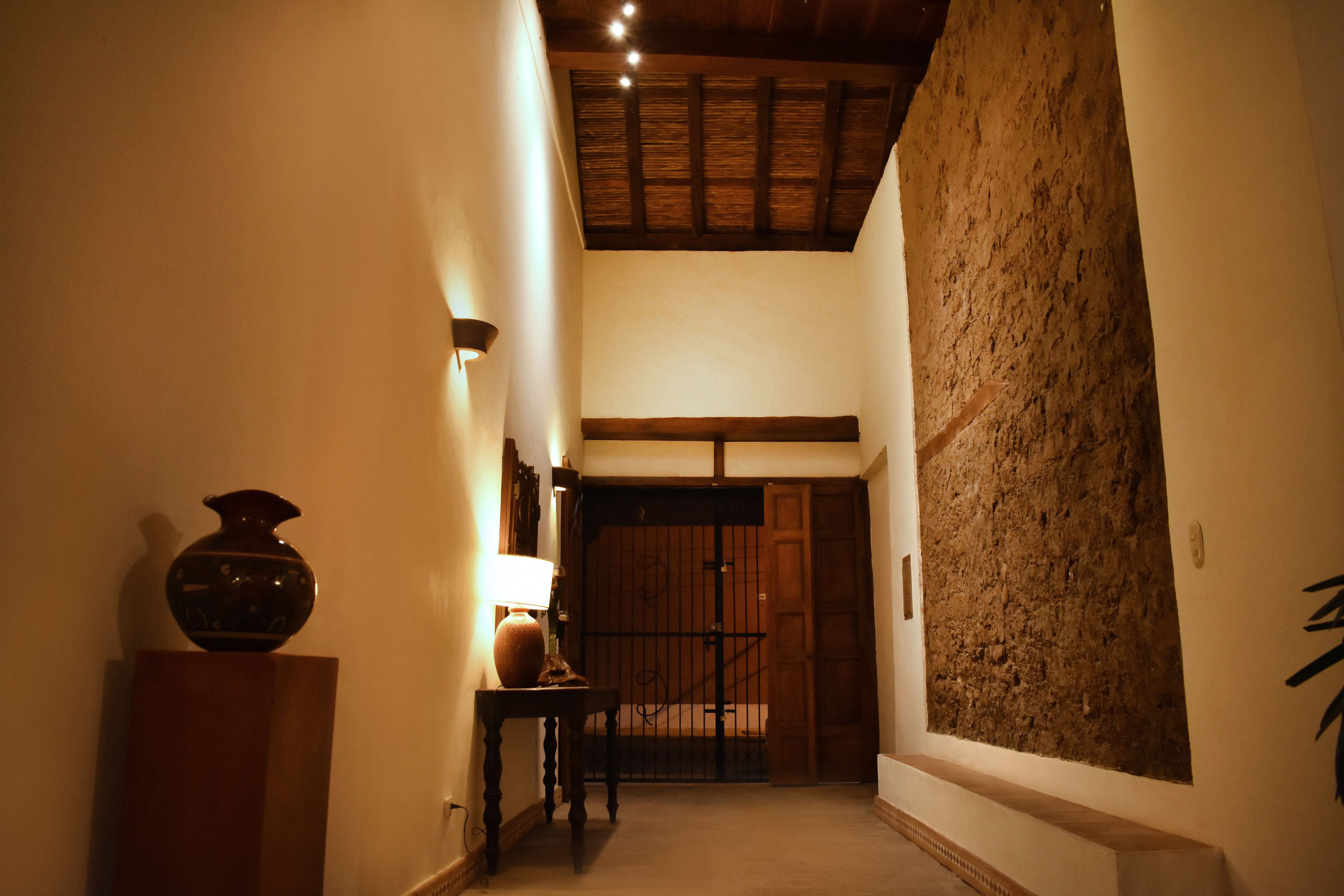 A narrow hallway with a wooden door at the end, a textured wall, and a small table with a lamp.
