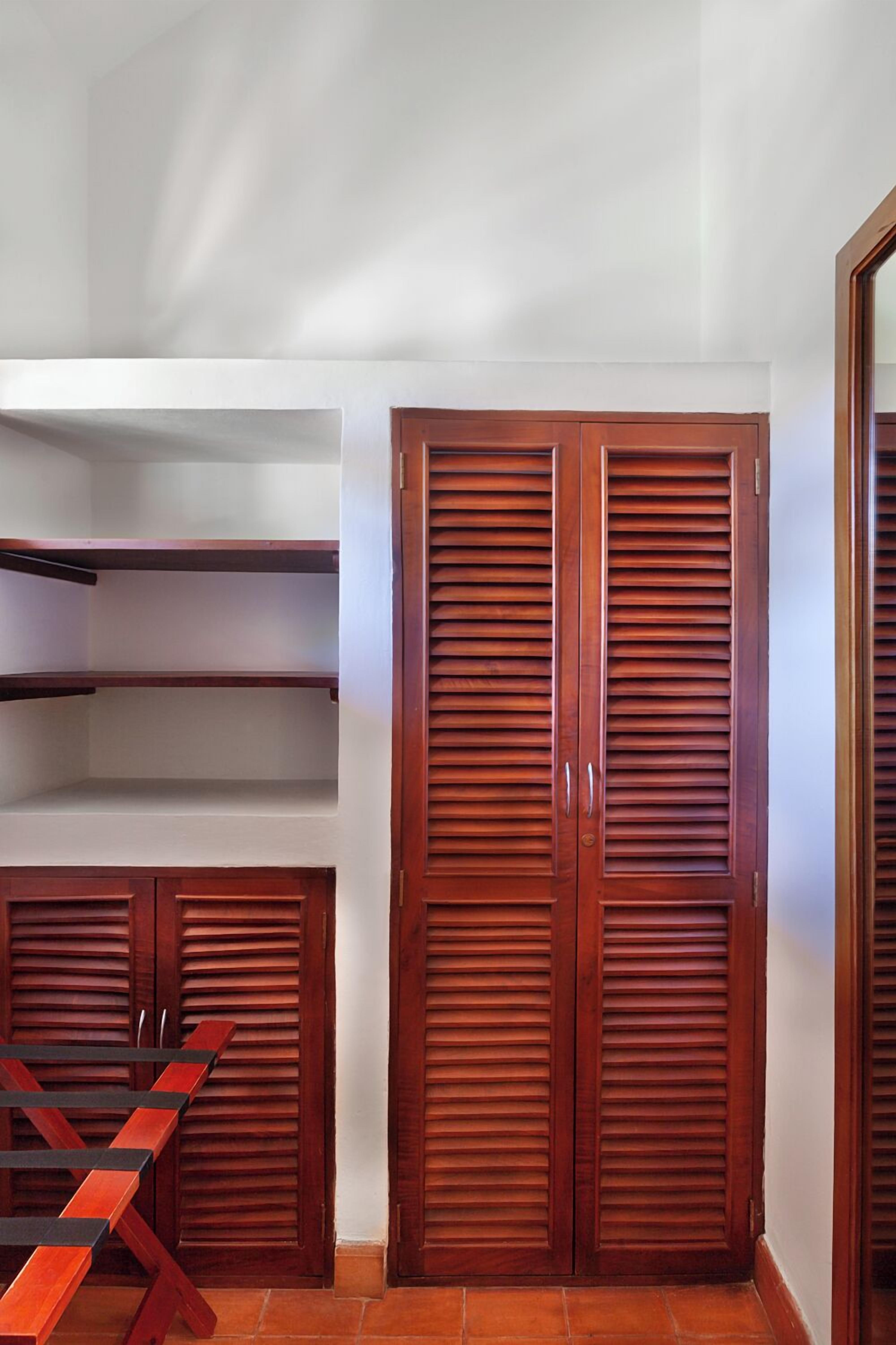 A room with a wooden wardrobe, a wooden bench, and a white wall.
