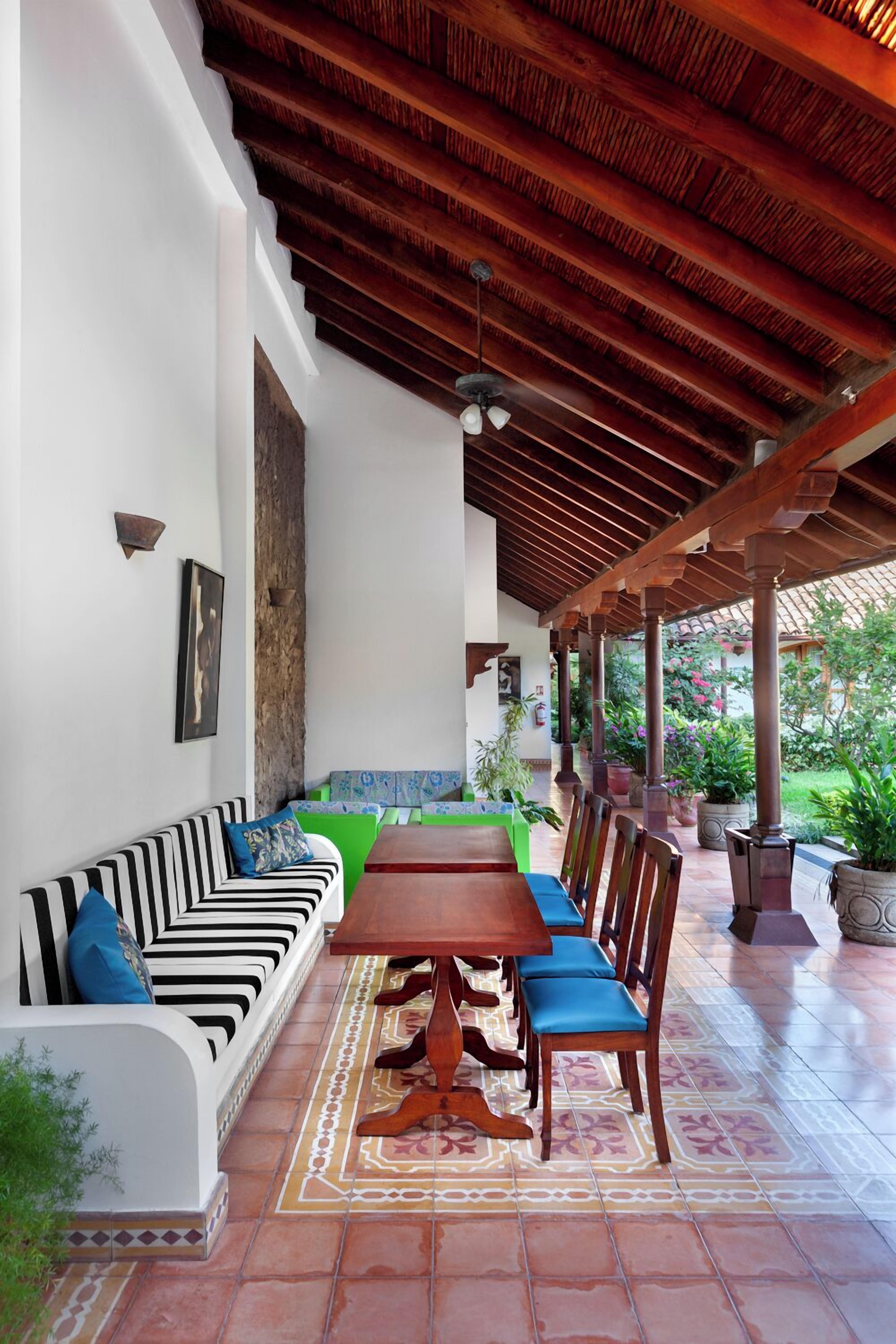 A covered outdoor dining area with a wooden table and chairs, a striped sofa, and a tiled floor.