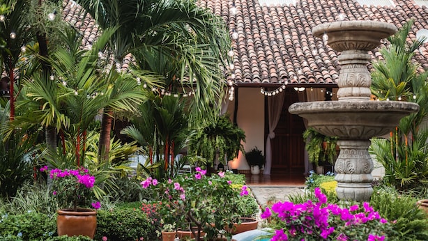 A courtyard with a fountain, potted plants, and a tiled roof.
