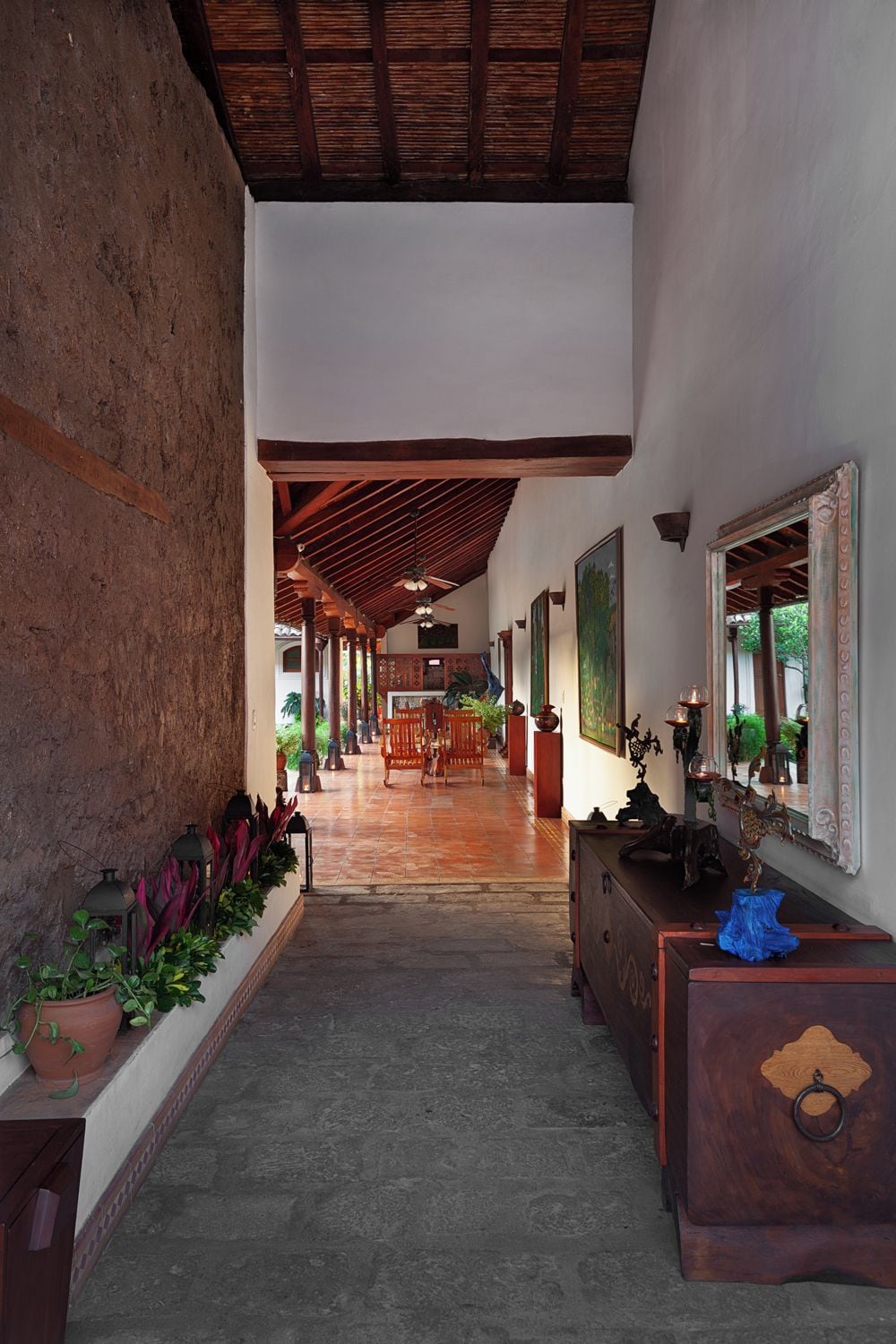 A corridor with a tiled floor, wooden ceiling beams, a bench, and a wall-mounted mirror.
