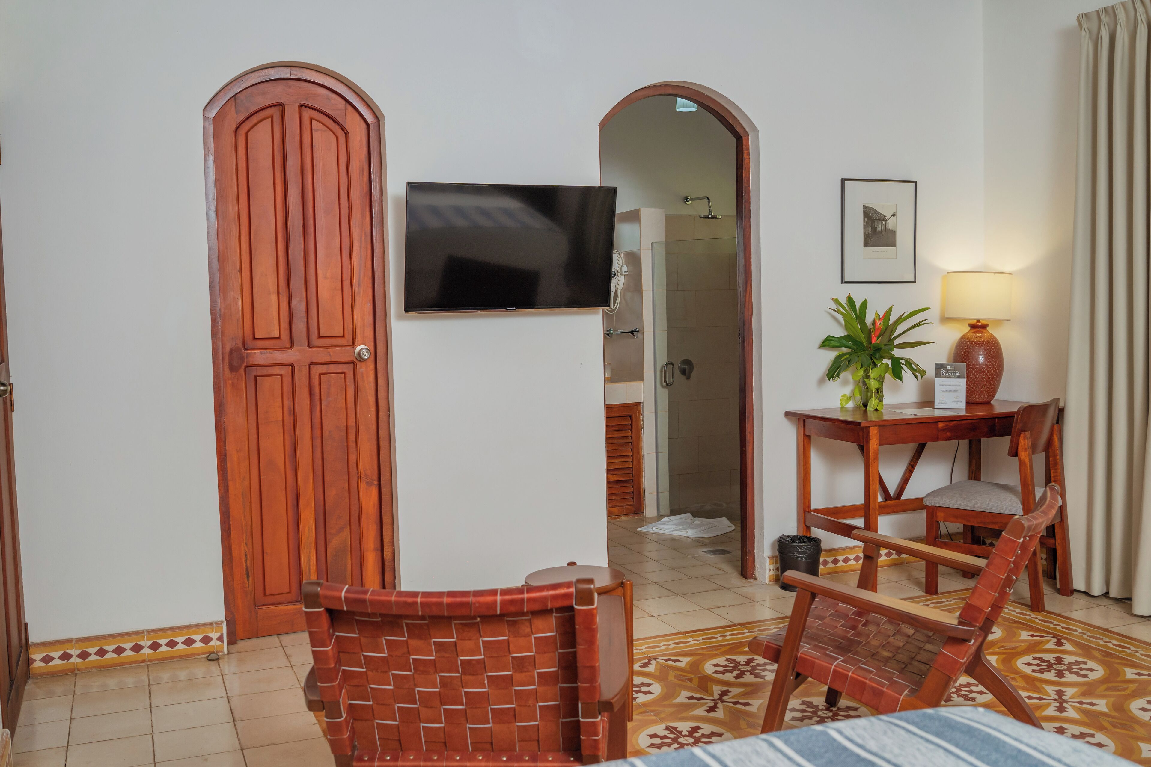 Une chambre d’hôtel avec une porte en bois, un téléviseur, une petite table avec une lampe, une chaise et un tapis à motifs.