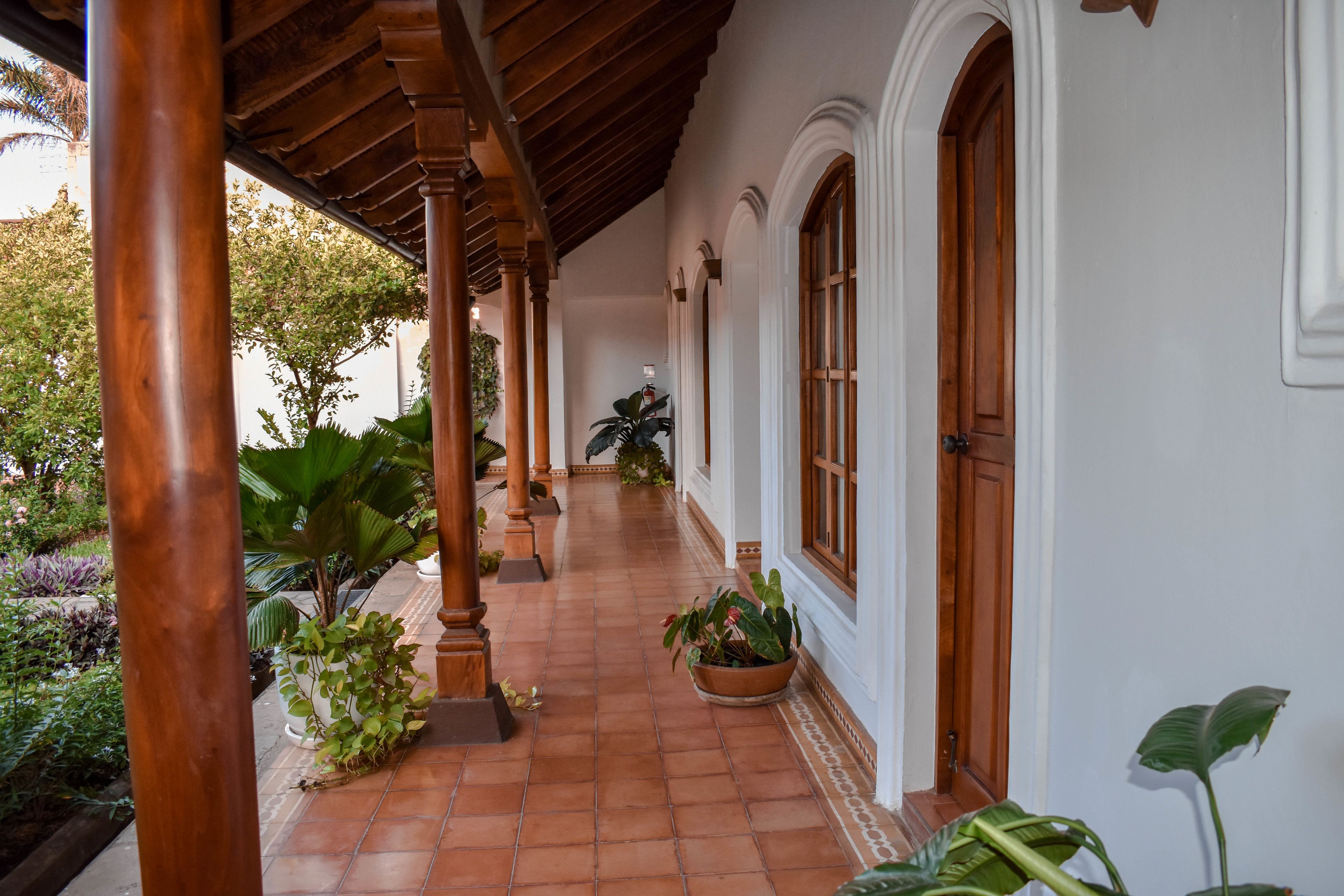 Un pasillo cubierto con suelo de baldosas, columnas de madera y plantas en macetas.