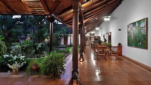 A covered walkway with tiled flooring, wooden benches, and potted plants.