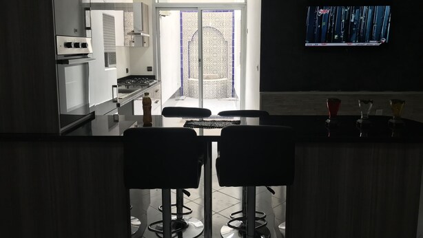 A modern kitchen with a bar area, a TV mounted on the wall, and a view of the outside through a glass door. - Luxury apartment in the heart of Casablanca (Casablanca)