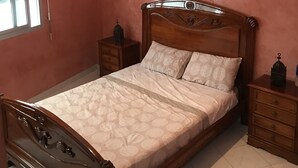 A bedroom with a wooden bed, a nightstand, a lamp, and a window with blinds. - Luxury apartment in the heart of Casablanca (Casablanca)