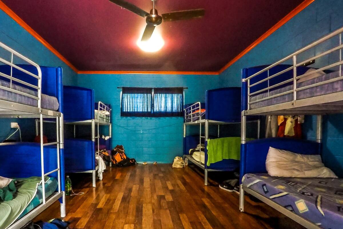 A dormitory room with bunk beds, wooden flooring, a ceiling fan, and a window with curtains.