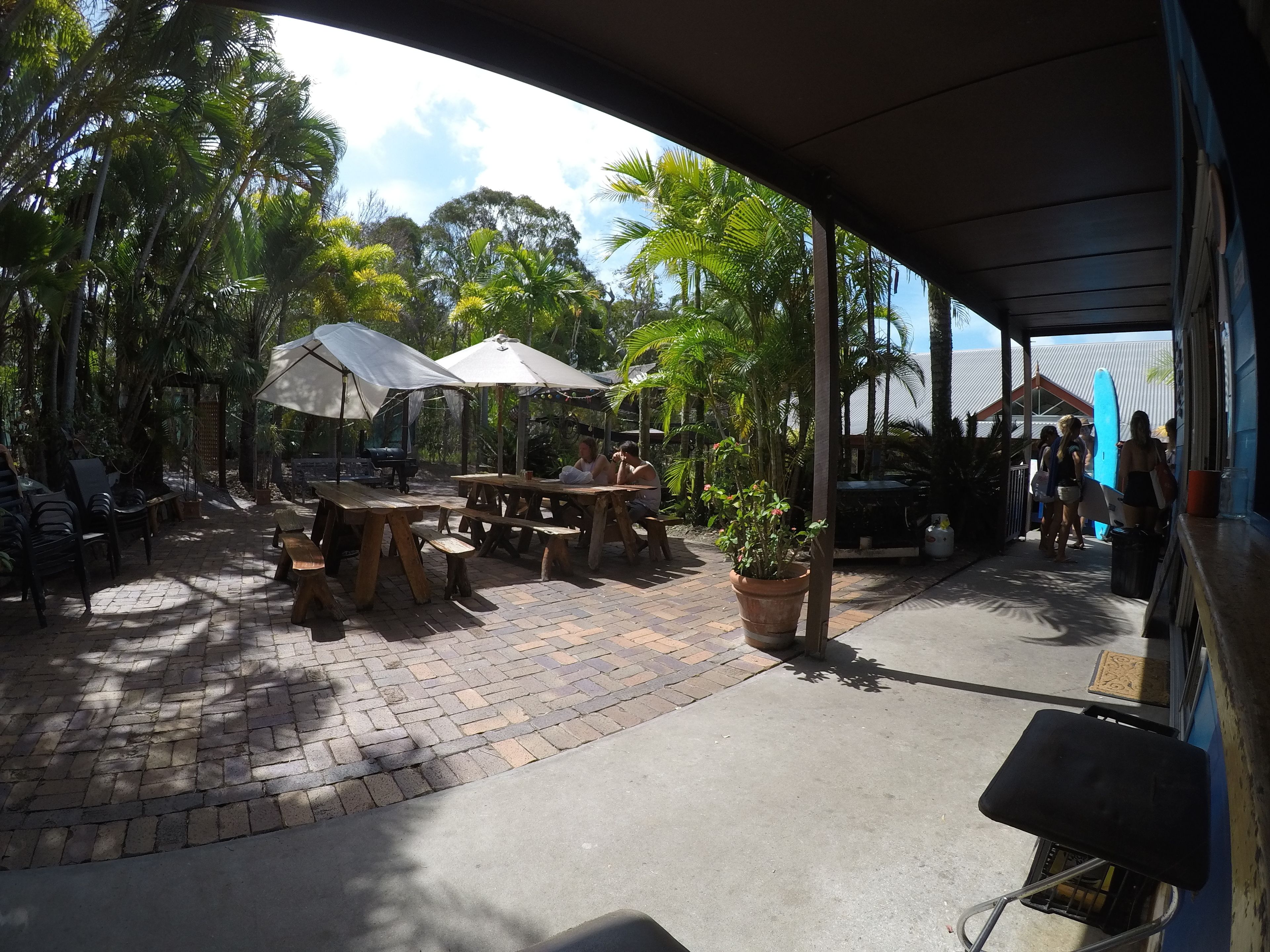 An outdoor patio area with wooden tables and chairs, umbrellas, and potted plants.