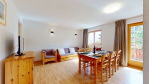 Ein gemütliches Zimmer mit einem Holzesstisch, Stühlen, einer Couch und einem Fernseher auf einem Holzschrank.