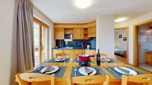 Ein Essbereich mit einem Holztisch, gedeckt für sechs Personen, einem roten Topf und einer Weinflasche.