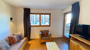 A cozy living room with a sofa, a chair, a TV, and a window with a view of buildings. - Pracondu 1 103 - OUTDOOR & FUN  apartment 6 pers (Haute-Nendaz)
