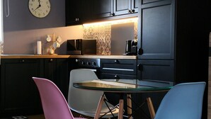 Een moderne keuken met donkere kastjes, een houten eettafel en kleurrijke stoelen.