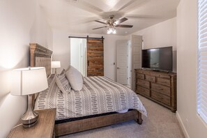 Un dormitorio con cama, televisión, cómoda, lámpara y ventilador de techo.