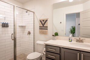 Un baño moderno con cabina de ducha de vidrio, inodoro, lavamanos con espejo y una pequeña planta en maceta.