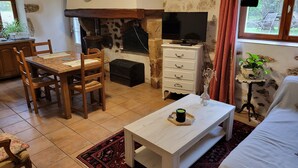 Ein gemütliches Wohnzimmer mit Kamin, Holzmöbeln, einem Fernseher und Blick ins Freie.
