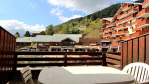 A wooden deck with a table and chairs, overlooking a village with buildings and a mountain in the background.