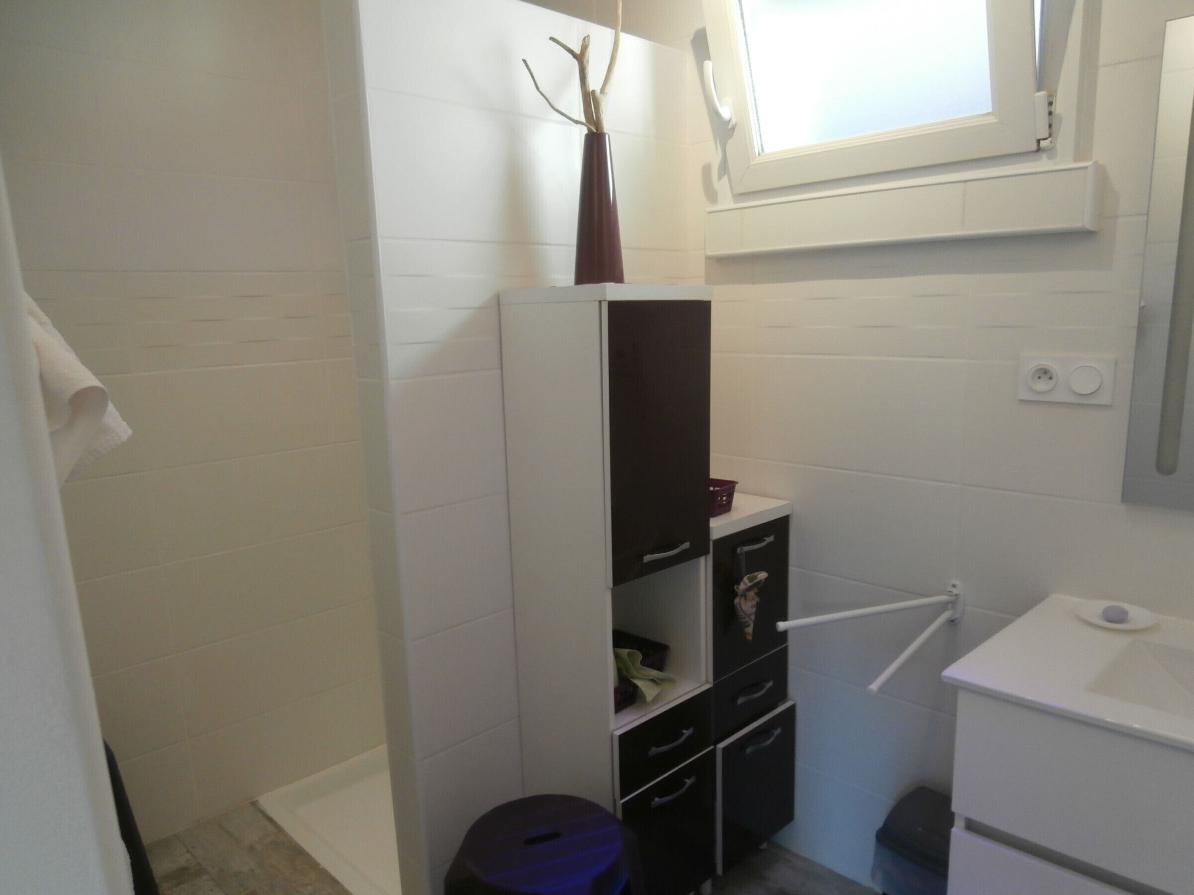 A compact bathroom with white tiled walls, a white sink, and a small window.