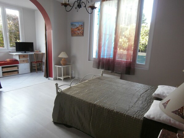 A bedroom with a bed, a desk, a chair, a television, and a window with curtains. - Charming Garden Level Home Near Capbreton Port, 3 Stars (Capbreton)