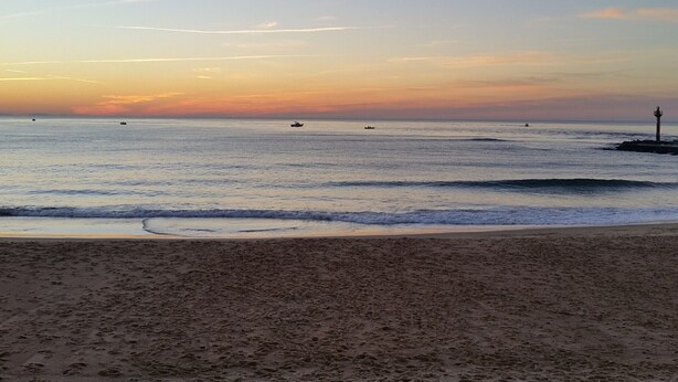 A beach with a lighthouse in the distance, calm sea, and a clear sky.
