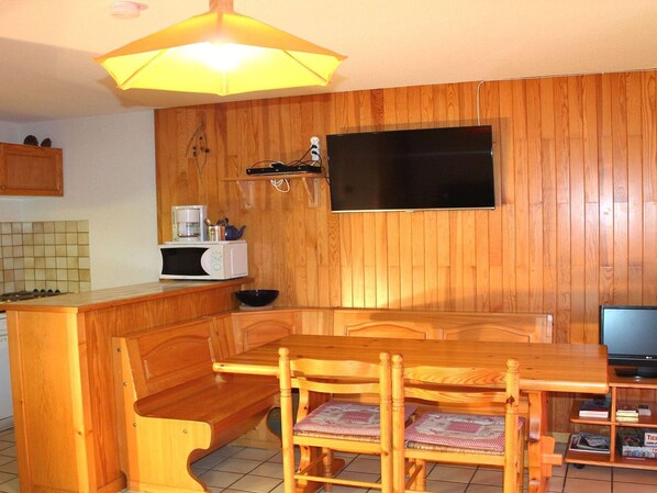 A compact kitchen with wooden paneling, a microwave, a coffee maker, and a television on a wooden stand.