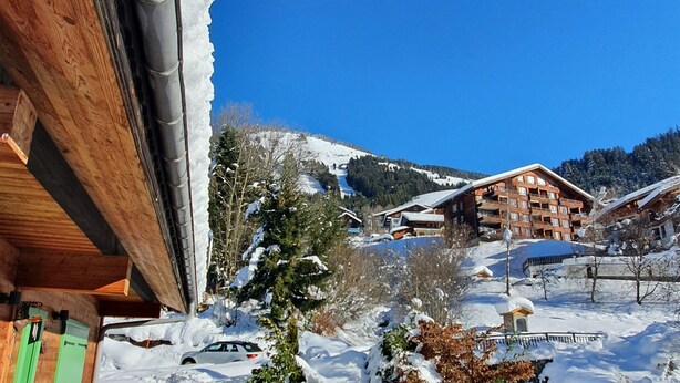 Ein hölzernes Gebäude mit einer Treppe, die zu einem Balkon führt, umgeben von schneebedecktem Boden und Bäumen.