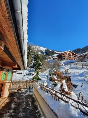 A wooden building with a staircase leading up to a balcony, surrounded by snow-covered ground and trees.