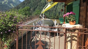 Ein Balkon mit Blick auf einen bewaldeten Berg, einem Tisch mit Stühlen und einem Blumentopf.