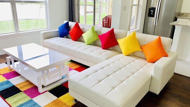 A modern living room with a white sofa, colorful cushions, a white coffee table, and a vibrant rug. - NEW Lakefront Disney Vacation Home (Kissimmee)