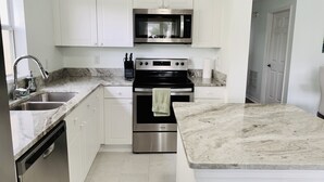 A modern kitchen with white cabinets, stainless steel appliances, a marble countertop, and a built-in oven. - NEW Lakefront Disney Vacation Home (Kissimmee)