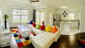 A modern living room with a white sofa, colorful cushions, a glass coffee table, and a vibrant rug. - NEW Lakefront Disney Vacation Home (Kissimmee)