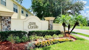 A Club Cortile sign with a landscaped garden featuring hedges, palm trees, and yellow flowers. - NEW Lakefront Disney Vacation Home (Kissimmee)
