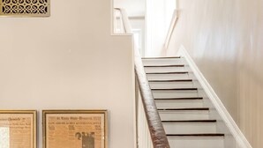 Eine Treppe mit weißen Balustern und einem hölzernen Geländer, neben einem Schrank mit Fischgrätmuster und einer Lampenfuß auf einem Stativ.