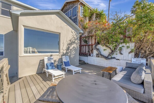 Un patio con un sofá blanco, dos sillones blancos, una mesa redonda y una terraza de madera.