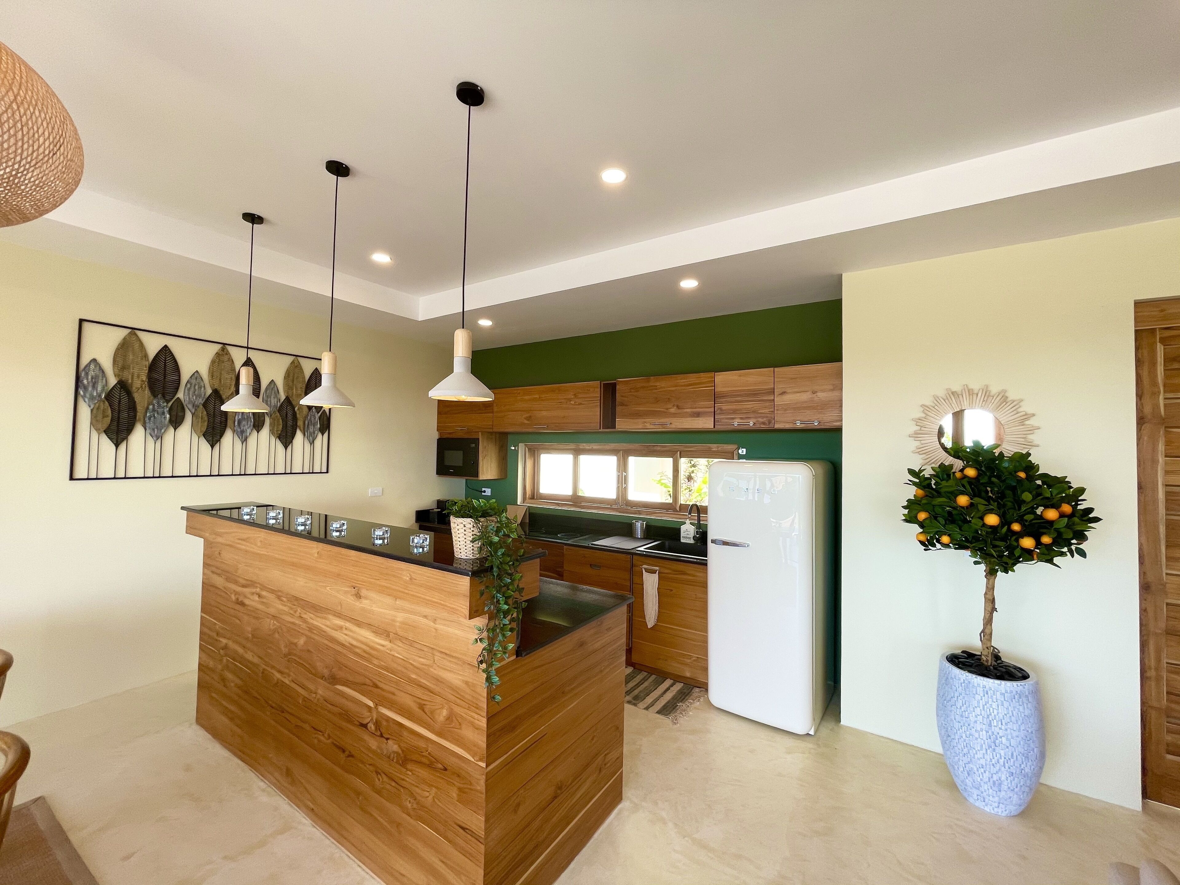 A modern kitchen with wooden cabinetry, a central island, pendant lighting, and a decorative plant.