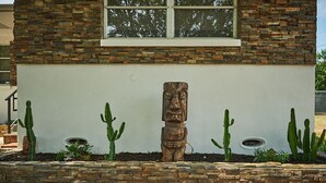 Ein modernes Haus mit einer Steinfassade, einem großen Fenster und einer Tiki-Statue aus Holz im Garten.