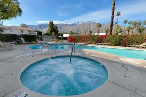 Un jacuzzi rodeado de sillones de descanso y una piscina, con montañas al fondo.