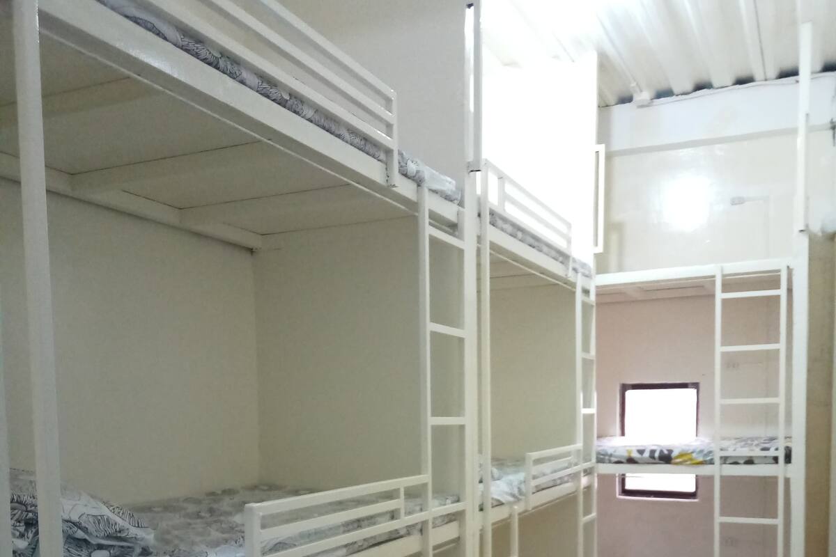 A dormitory room with bunk beds, wooden flooring, and a window providing natural light.