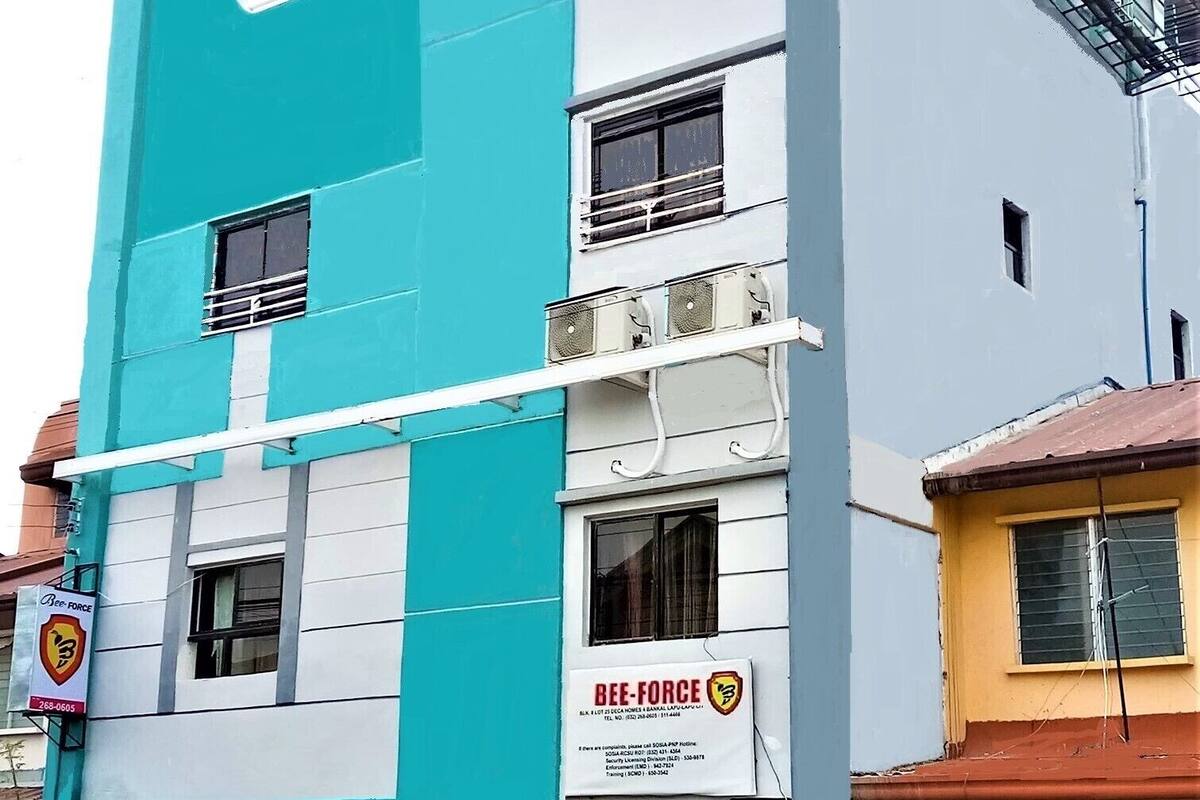 A multi-story building with a blue and white facade, a visible sign for 'Bee-Force', and a parked motorcycle in front.