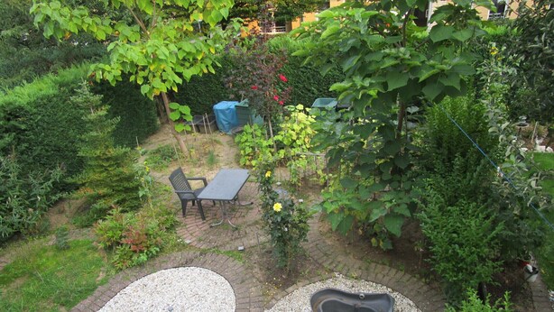 Un giardino con area pavimentata, tavolo e sedie, e un piccolo stagno.